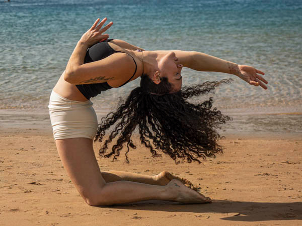 Yoga Keishla haciendo pose de yoga sobre la arena con el mar de la playa de Las Teresitas de fondo