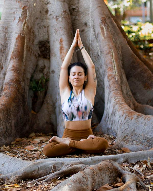 Breathwork como herramienta Keishla en pose de estiramiento para respiración con fondo de un árbol del parque García Sanabria